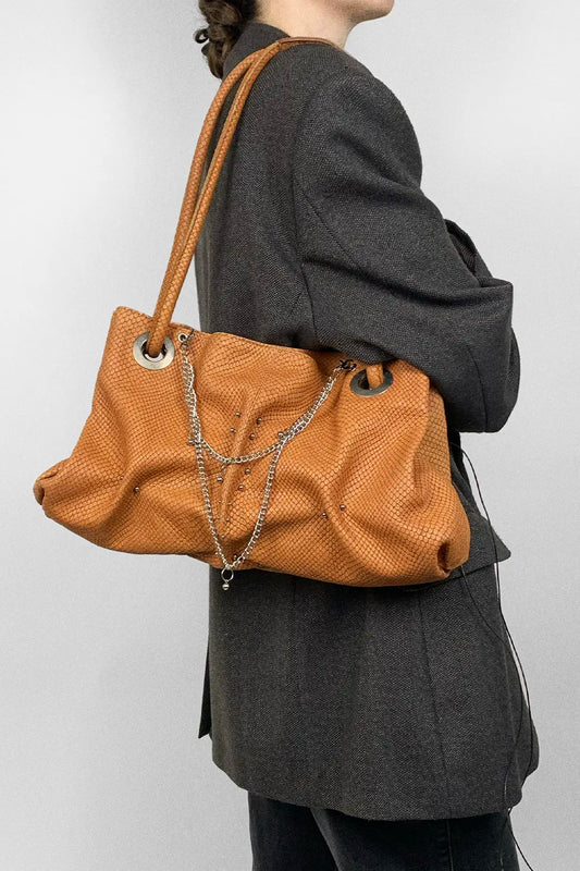 Person wearing amber textured handbag with a chain and piercing detail on a plain background