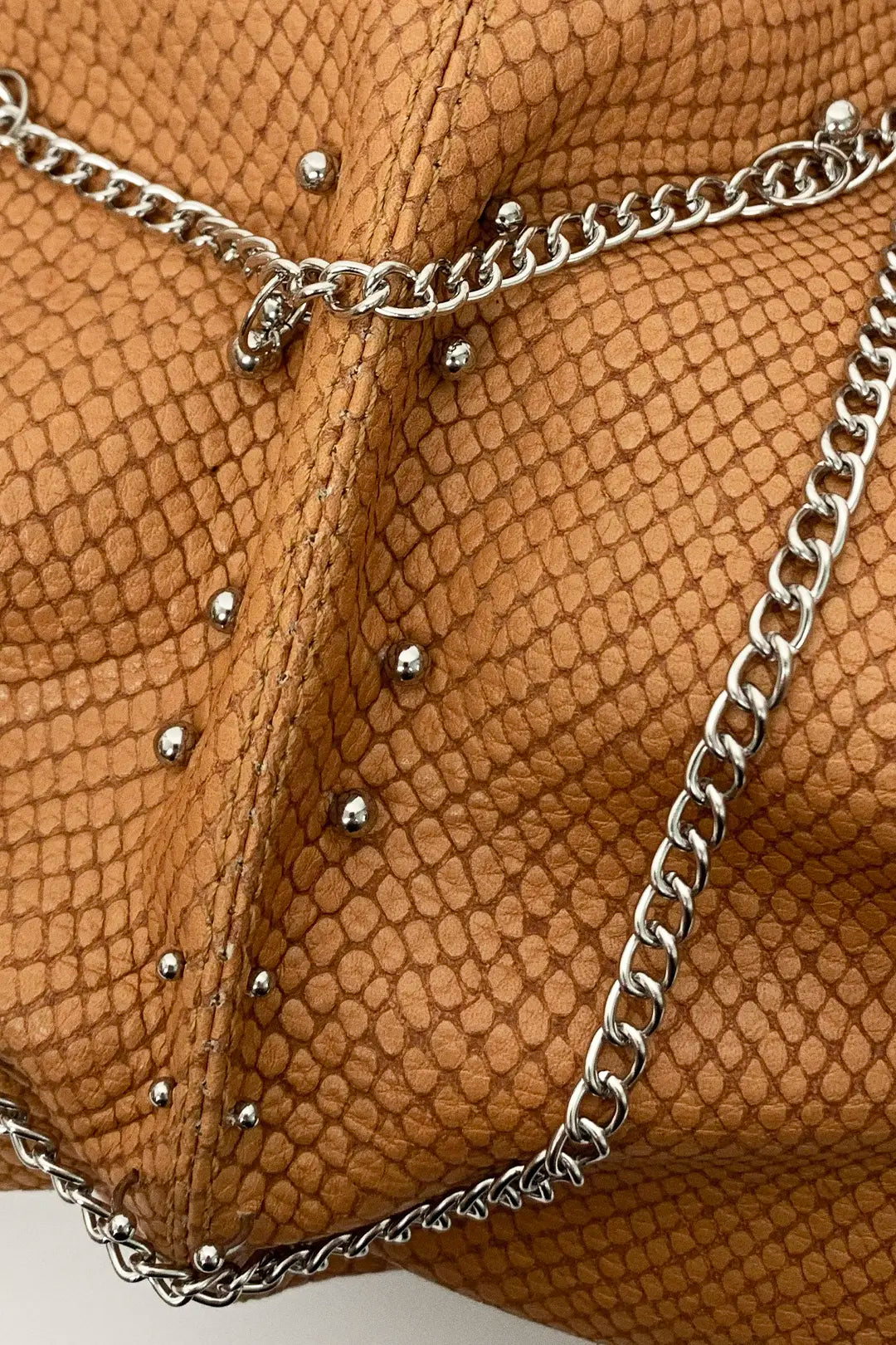 Close-up of leather textured handbag with silver chain and piercings
