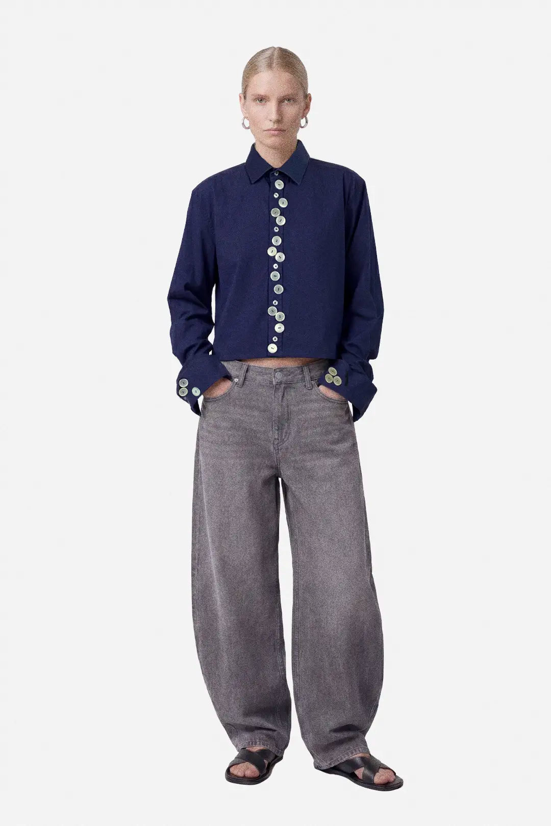 Person wearing a navy blue button-up shirt and gray pants on a white background
