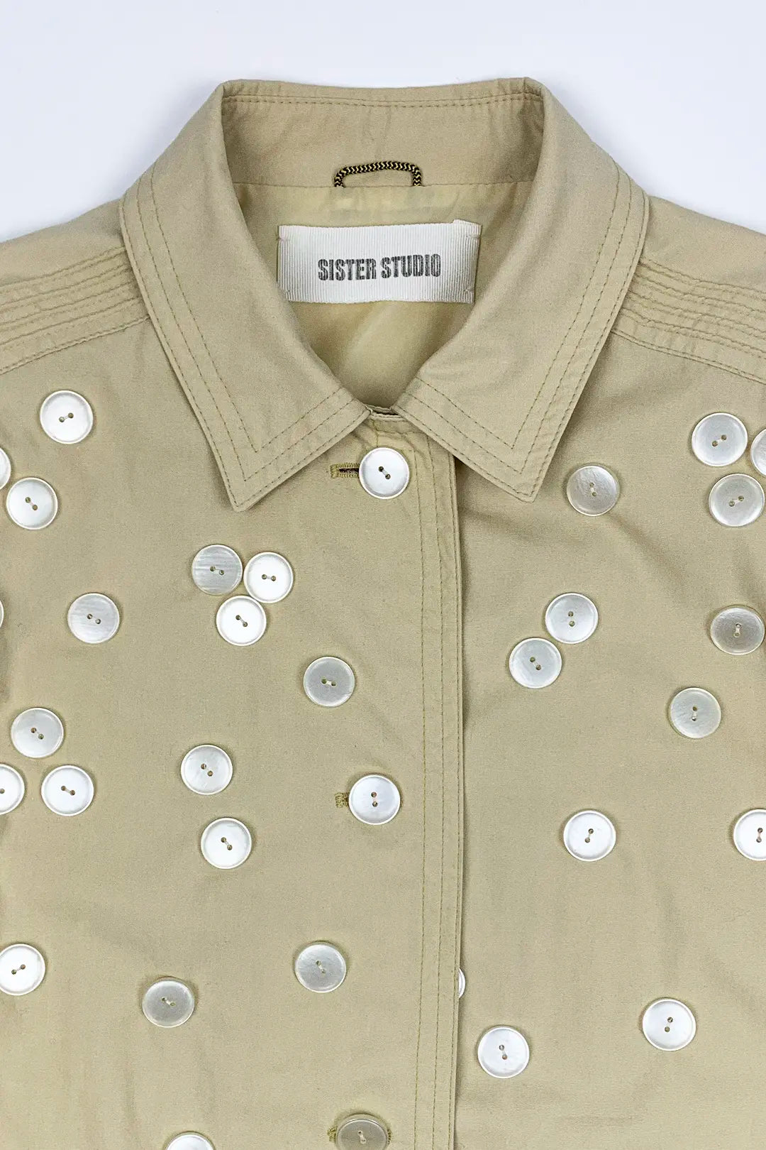 Beige jacket with button embellishments on a white background, featuring 'Sister Studio' label.