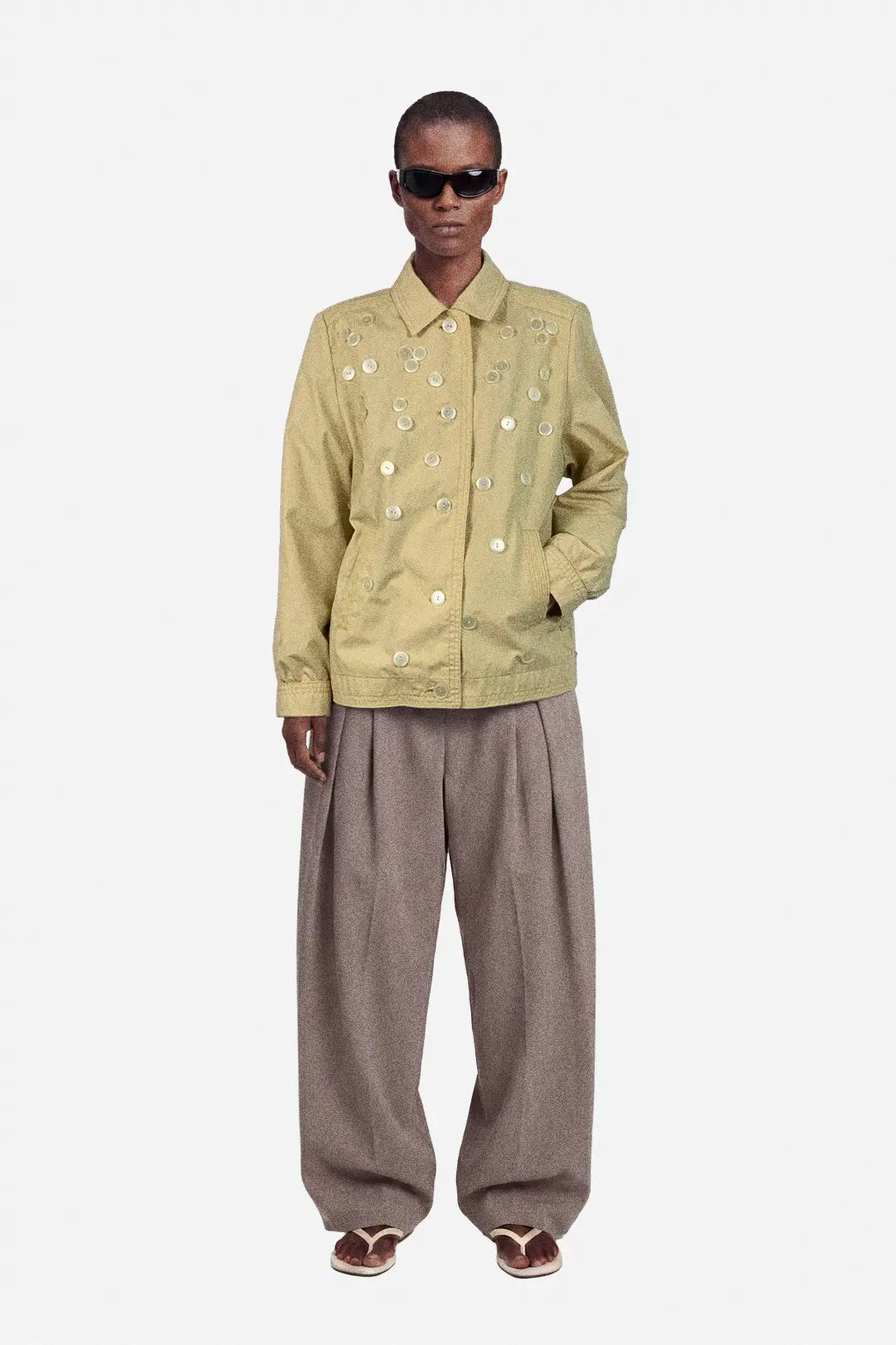 Person wearing a beige jacket and brown pants on a white background
