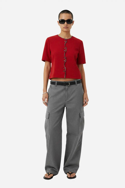 A model wearing a red short-sleeve cropped top with decorative dark buttons down the front, paired with gray wide-leg cargo pants and black sunglasses, standing against a light gray background.