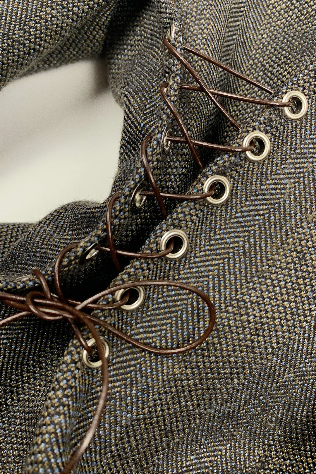 Close-up of a textured fabric surface with metal eyelets and leather laces.