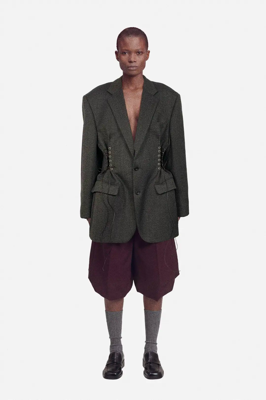 Person wearing a dark brown blazer and maroon shorts on a white background