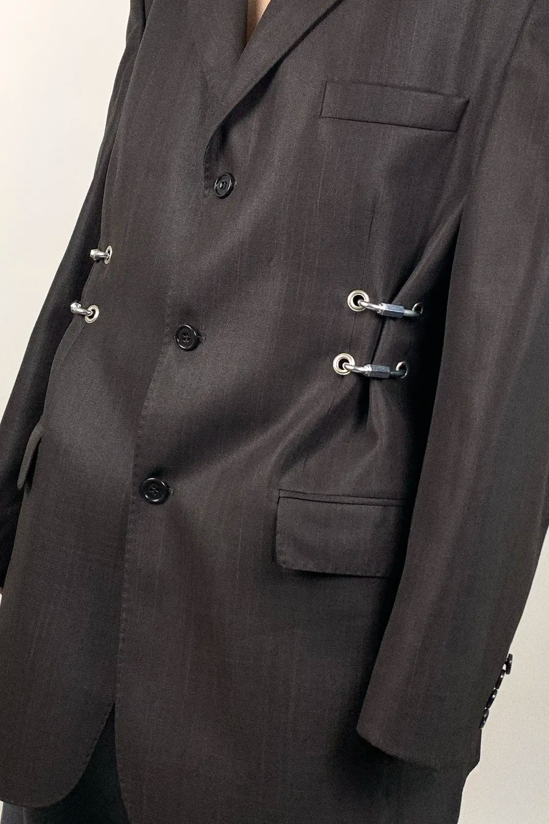Dark brown suit jacket with hardware details on a neutral background