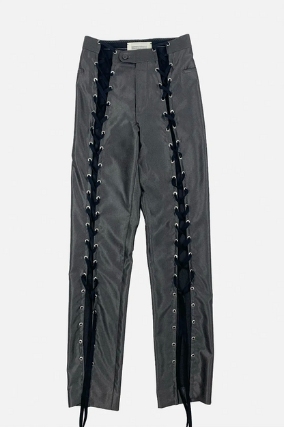 Dark gray pants featuring prominent black lace-up detailing running down both sides with silver metal eyelets, shown against a light gray background.