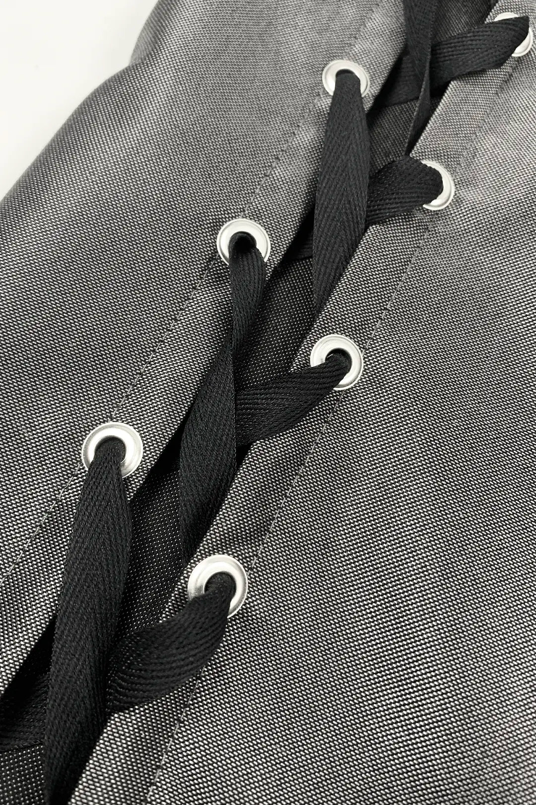Close-up of a gray woven textile with black laces threaded through white eyelets.