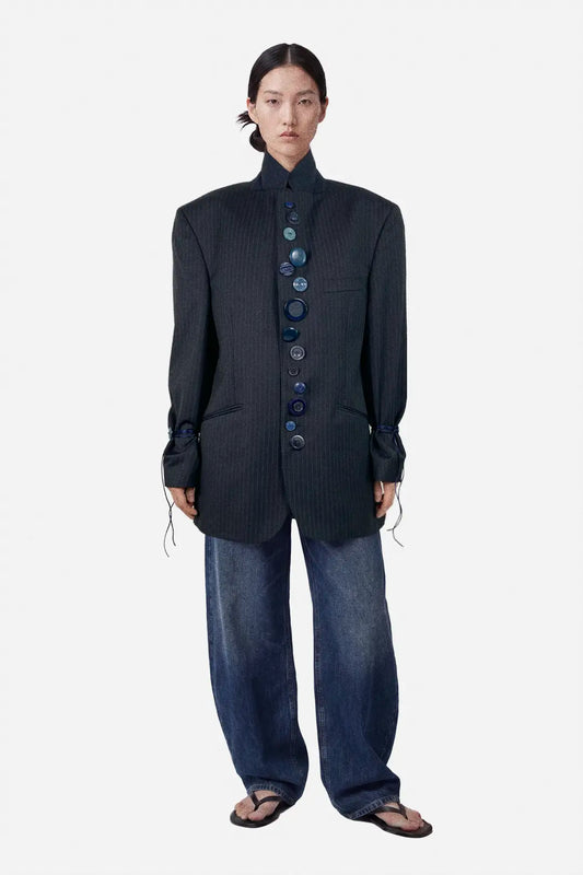 Person wearing a dark blue textured jacket with button details and wide-leg jeans on a white background