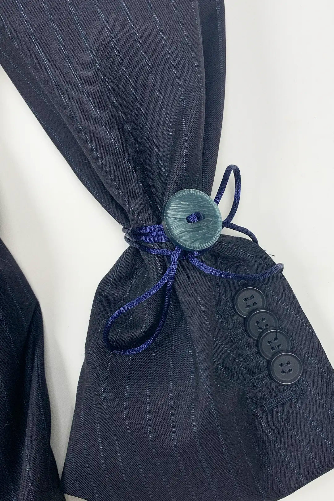Navy pinstripe suit jacket with a decorative button and blue ribbon on a white background