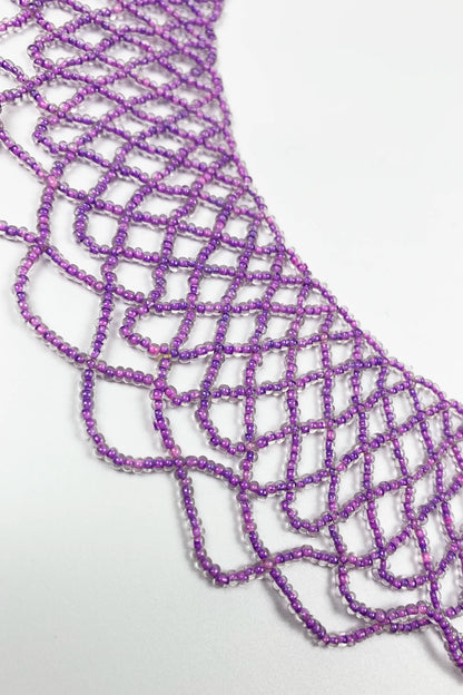 A close-up of a purple beaded lace trim with an openwork geometric pattern, laid flat on a white background.