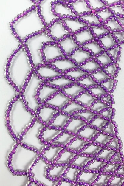 Purple iridescent seed beads arranged in a loose, tangled loop pattern on a plain white background.