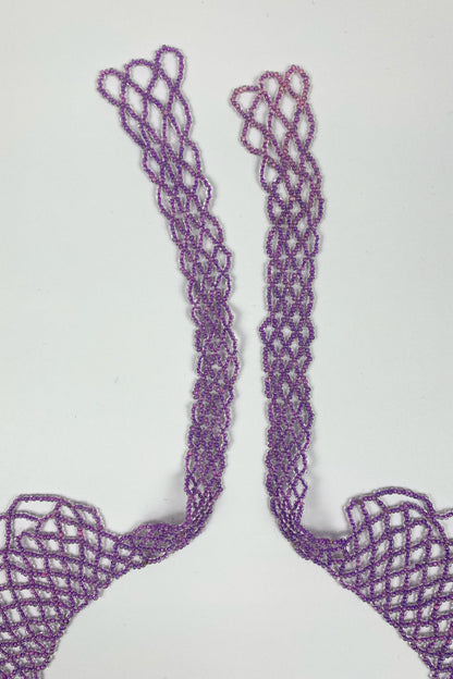 A pair of lavender purple crochet or lace trim pieces with a textured openwork pattern, laid flat on a light gray background.