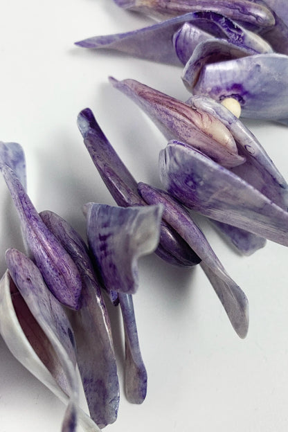 Purple and lavender seashell beads with natural ridges, arranged on a clean white background.
