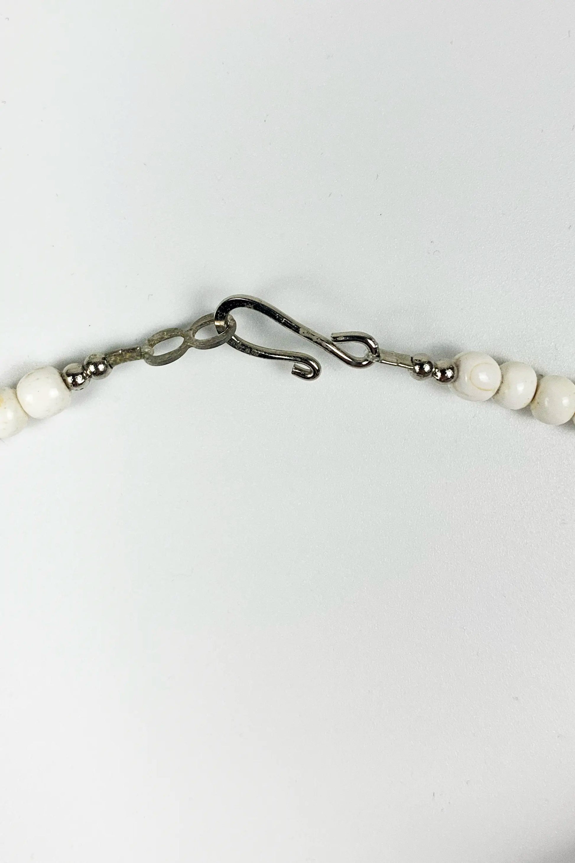 A close-up of a beaded necklace with white round beads and a dark metal lobster clasp on a plain white background.