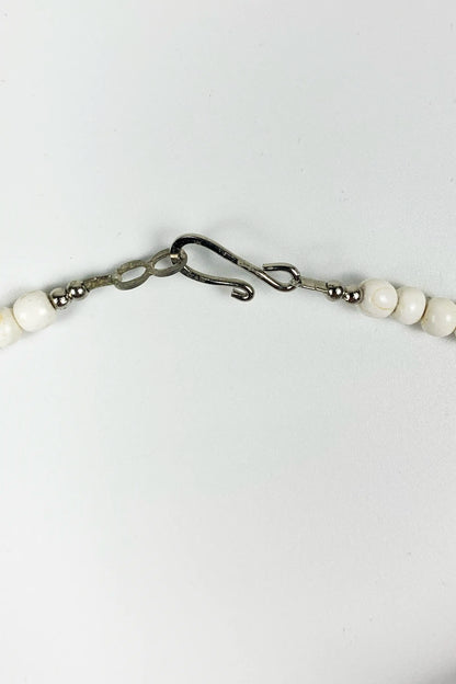 A close-up of a beaded necklace with white round beads and a dark metal lobster clasp on a plain white background.