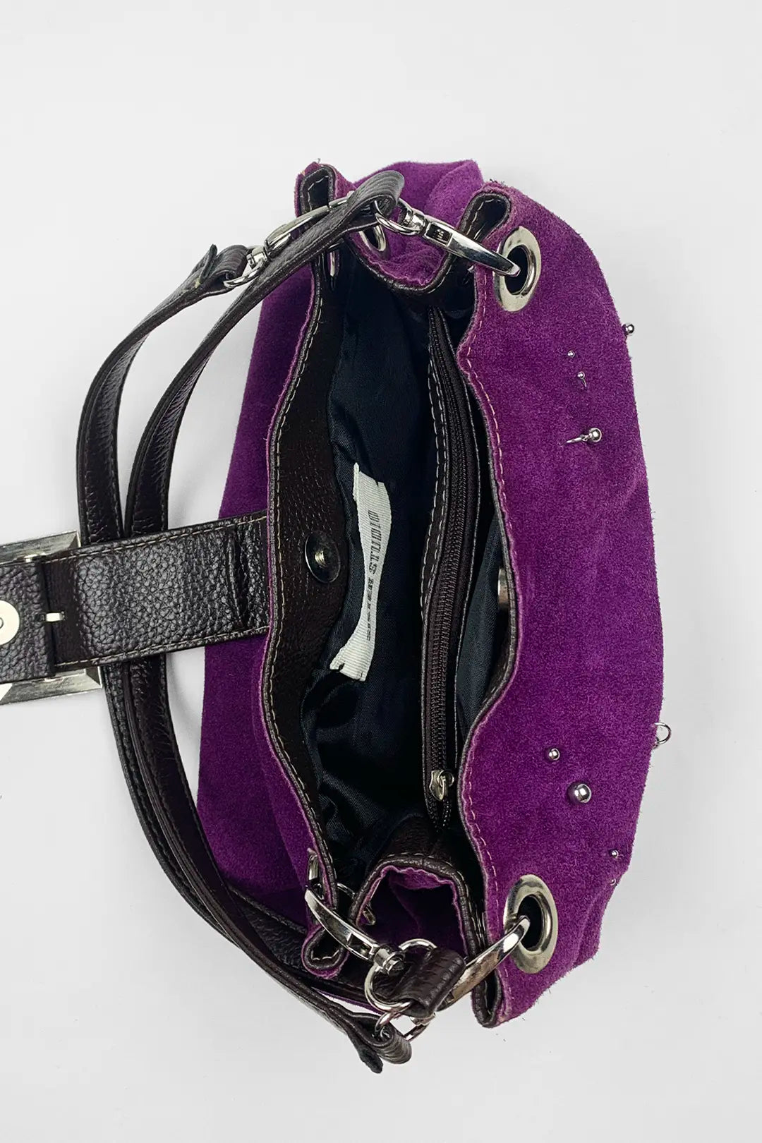 A purple suede shoulder bag with black leather straps and silver-tone hardware, shown from an overhead angle against a white background.