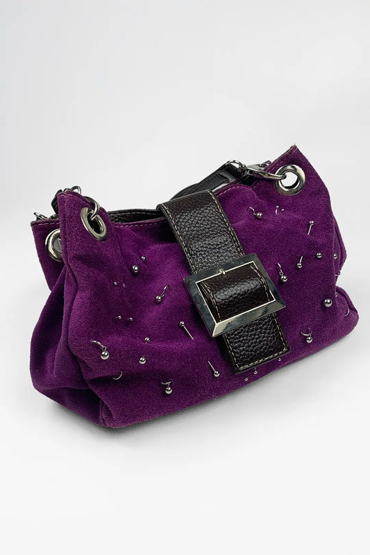A purple suede shoulder bag with a black faux-leather strap and silver-tone studs, photographed on a light gray background.