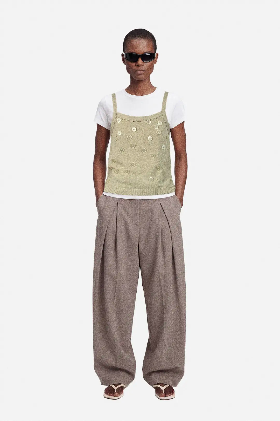 Person wearing a beige upcycled top with button details and white shirt on a white background