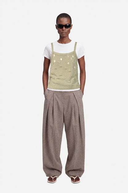 Person wearing a beige upcycled top with button details and white shirt on a white background