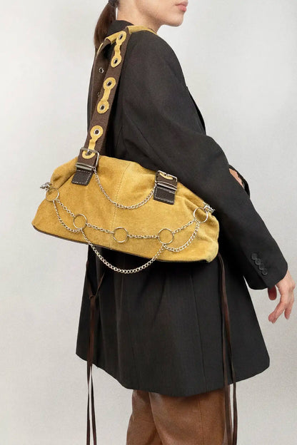 Person wearing a mustard yellow handbag with chain details on a plain background