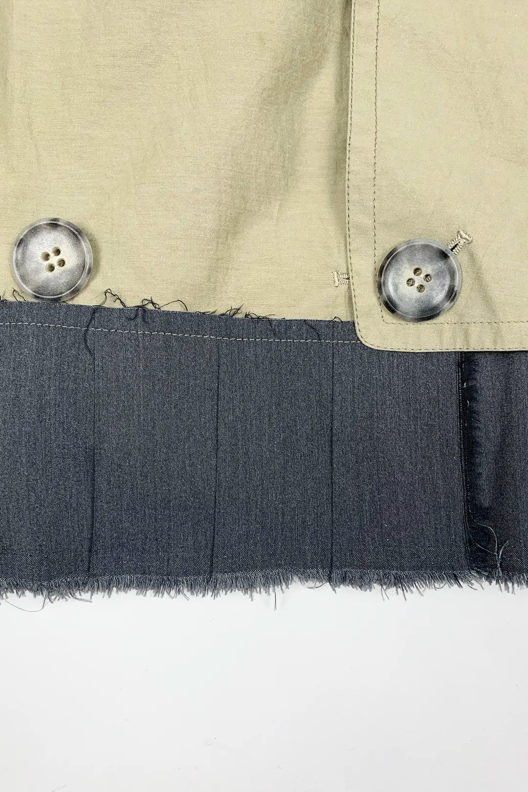 Close-up of a beige jacket with buttons and a dark fabric trim on a white background
